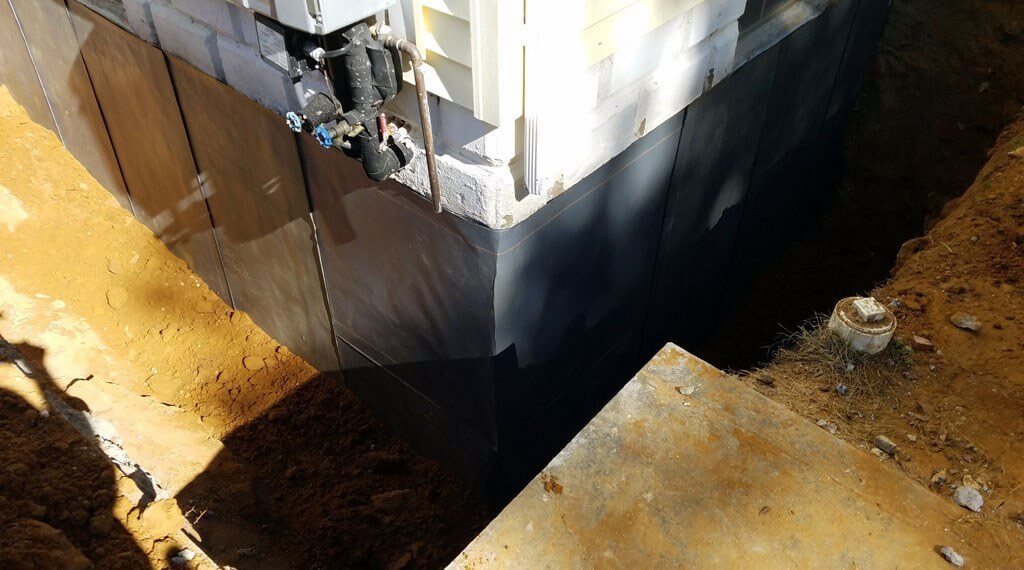 Exterior of foundation exposed to show waterproofing and dirt around base of home