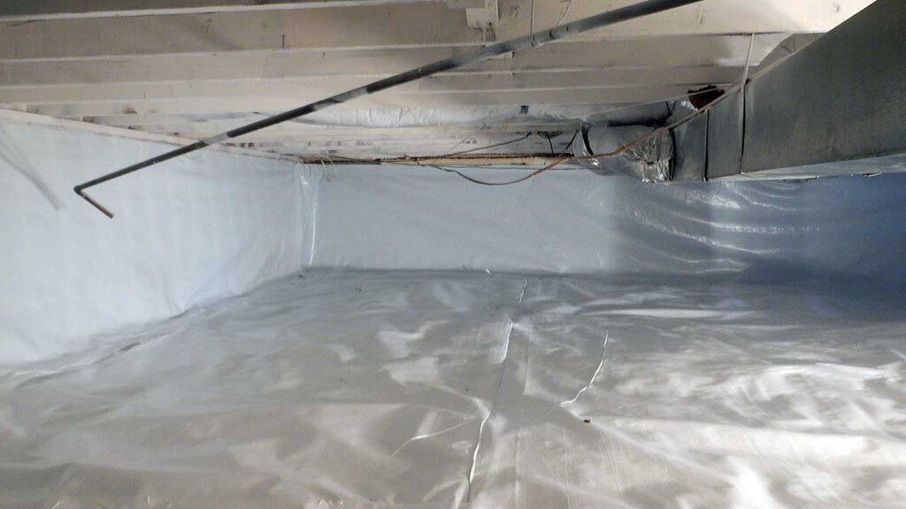 Home crawl space with wood foundation, insulation, and pipes showing