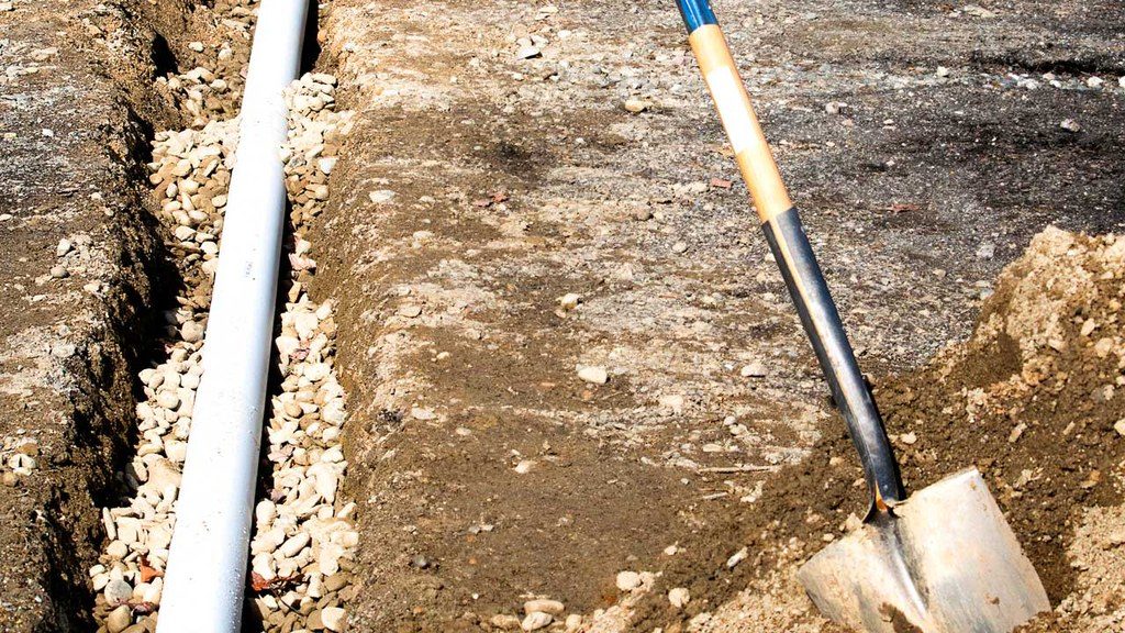 Open trench in the ground with pipe next to shovel sticking out of the dirt