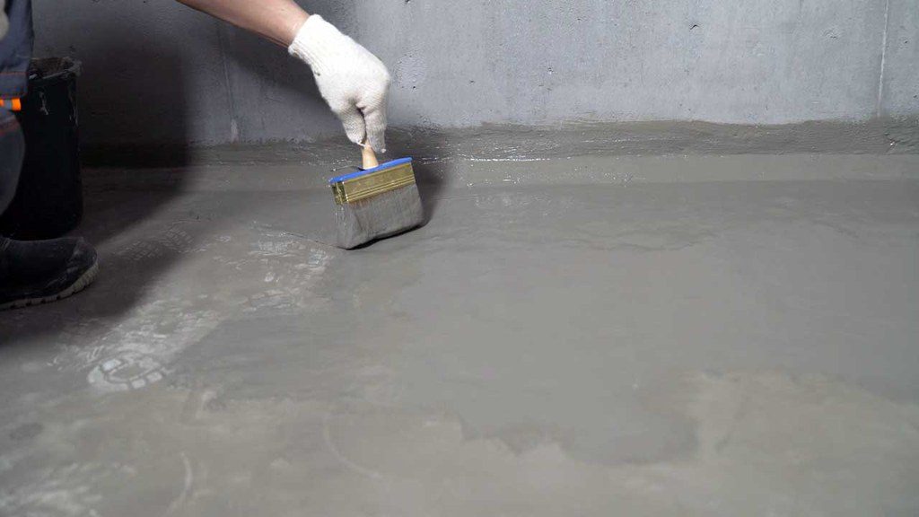 Dry Tech Waterproofing Solutions employee spreading concrete on basement floor