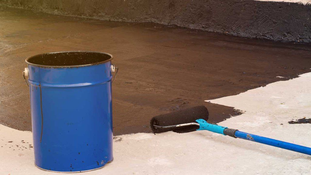 Waterproof sealant partially spread on floor next to bucket and roller