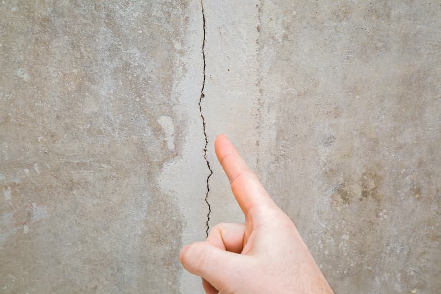 Person pointing at a crack in a building foundation