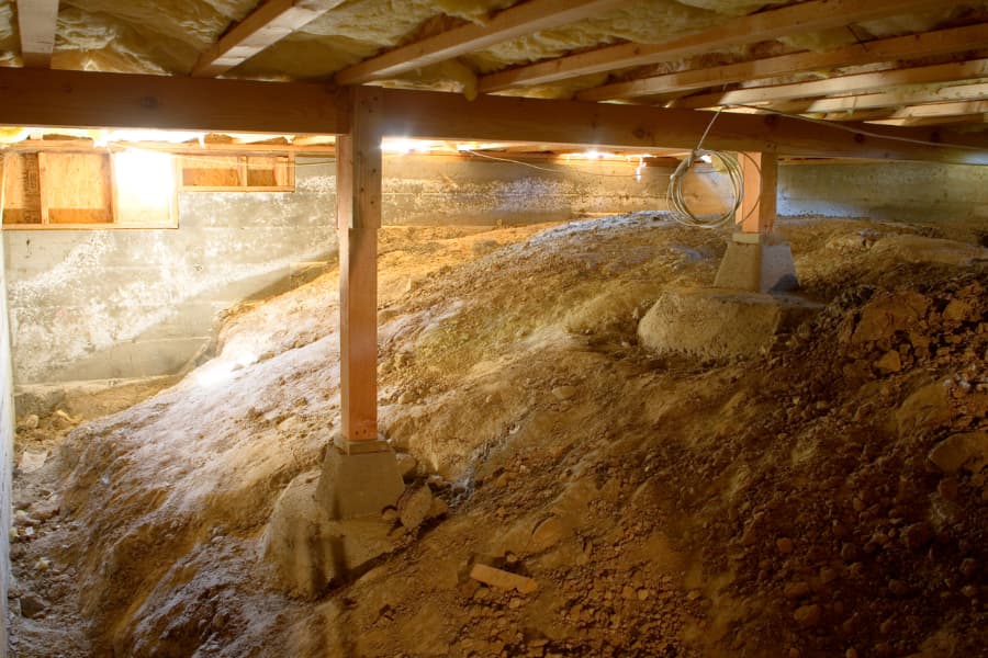 Crawl space with dirt and wooden support beams under home