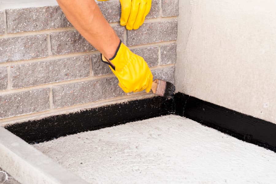 Worker applying bitumen coating to house foundation
